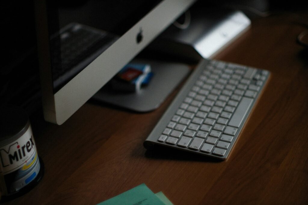 “Apple iMac and wireless keyboard on a wooden desk – author’s workspace for writing books and answering FAQ questions.”